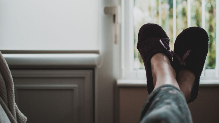 person sitting on a chair facing a window with their feet up cladded in comfy slippers