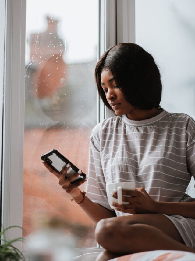 woman-looking-through-phone-sitting-window